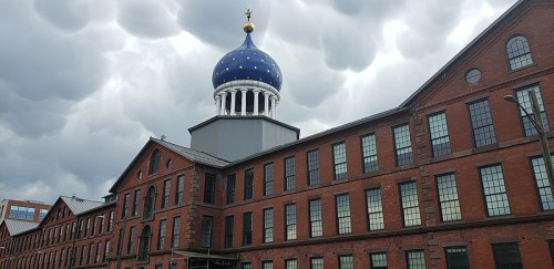 Historic red brick building with large windows and a distinctive blue dome under a cloudy sky.