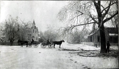 A vintage winter scene with horse-drawn carriages on an icy street, surrounded by snow-covered trees and buildings.