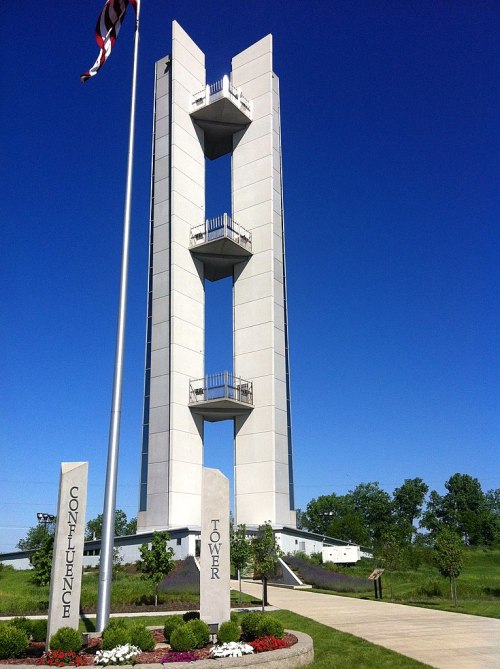 A tall, modern tower with three levels, surrounded by greenery and marked by stone pillars reading "Confluence" and "Tower."