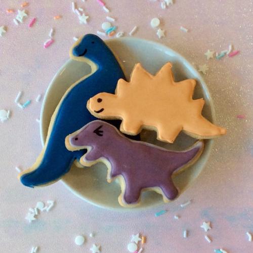 Three colorful dinosaur-shaped cookies on a plate, surrounded by pastel confetti.