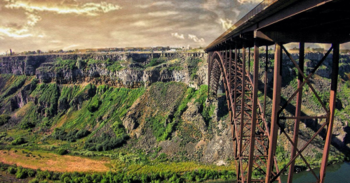 A panoramic view of a bridge spanning a rocky canyon, surrounded by lush greenery and a river below.