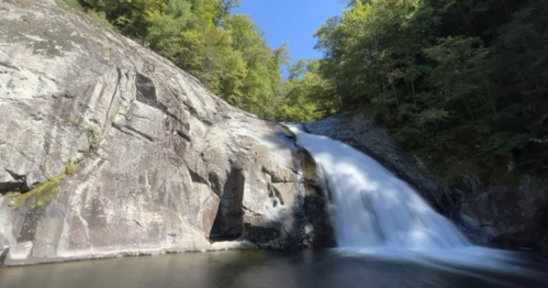 A serene waterfall cascading over rocky cliffs, surrounded by lush green trees under a clear blue sky.