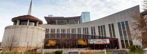 Modern building with a curved facade, featuring large windows and a distinctive roof, surrounded by trees and grass.