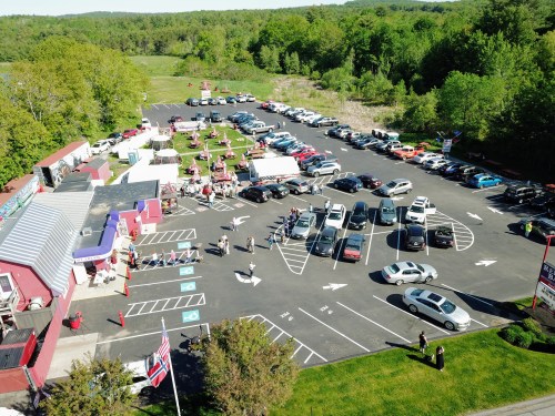 Aerial view of a busy parking lot with various cars, surrounded by greenery and event tents.