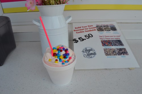 A cup of ice cream topped with colorful sprinkles and a pink straw, next to a menu and a flower pot.