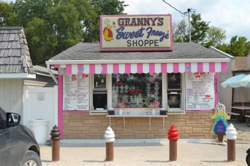 A colorful ice cream shop with a pink exterior, striped awning, and a menu of treats displayed outside.
