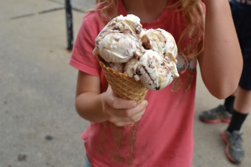 A child holds a large ice cream cone with multiple scoops of chocolate and vanilla flavors.