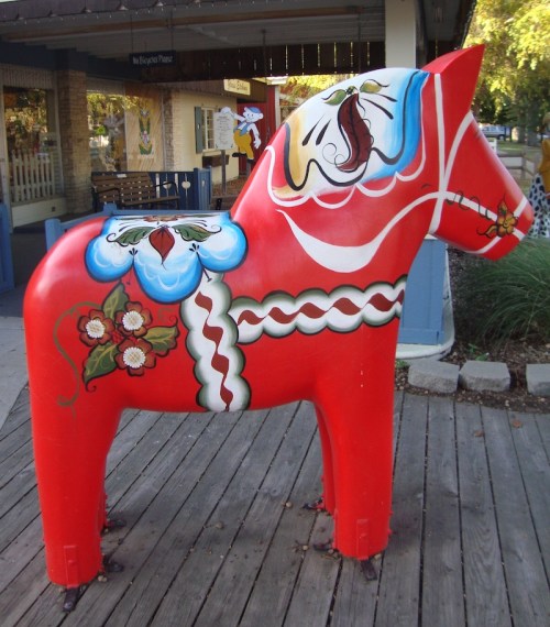 A colorful, painted wooden horse statue with floral designs, standing on a wooden deck.