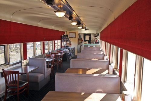 Interior of a diner with red curtains, wooden tables, and booths, featuring large windows for natural light.