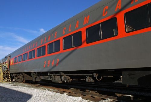 A vintage train car with a gray exterior and orange accents, labeled "Seattle Dan's Clam Car," parked on tracks.