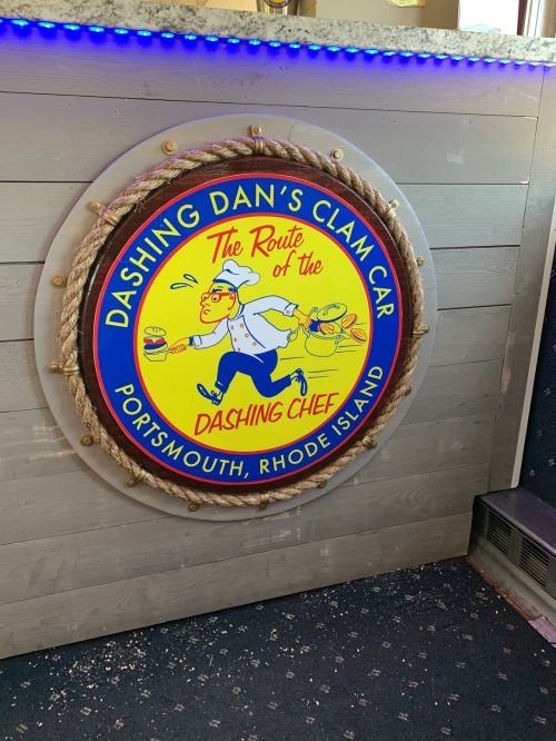 Sign for "Dashing Dan's Clam Car" featuring a chef with clam dishes, located in Portsmouth, Rhode Island.