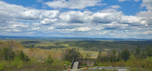 A scenic view of rolling hills and valleys under a partly cloudy sky, with a wooden overlook in the foreground.