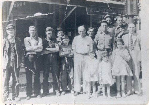 A black-and-white photo of a group of men, women, and children standing together outside a building.