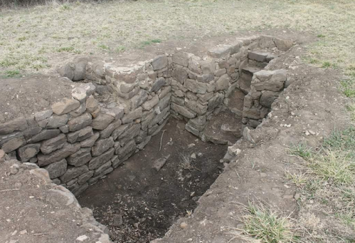 A rectangular stone structure partially filled with dirt, surrounded by grass.