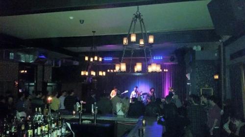 A lively bar scene with a band performing on stage, dim lighting, and an audience enjoying the music.