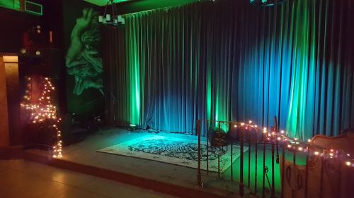 A dimly lit stage with green and blue lights, draped curtains, and decorative string lights.
