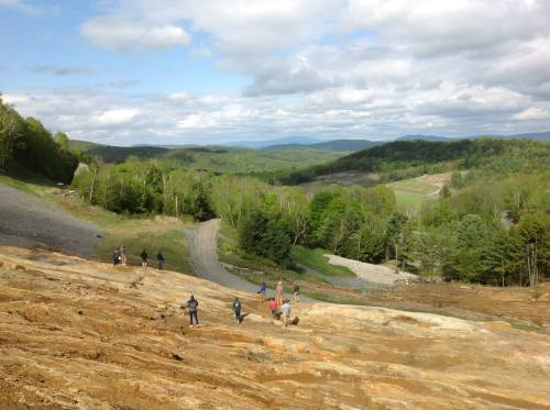 A group of hikers explores a rocky landscape with lush green hills and a cloudy sky in the background.