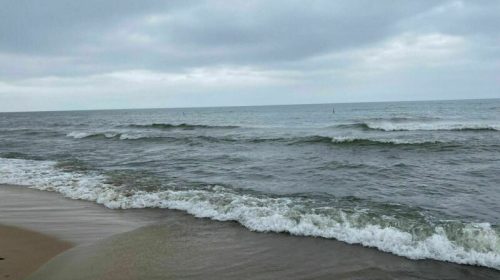 A calm beach scene with gentle waves lapping at the shore under a cloudy sky.