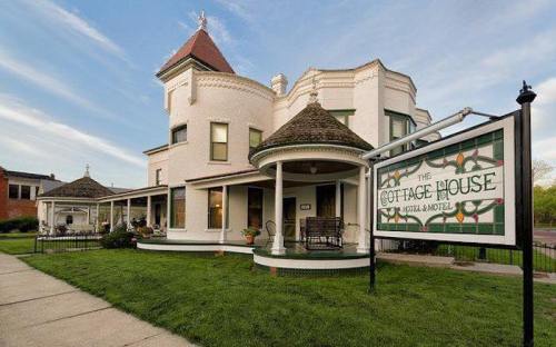 A charming white Victorian-style house with a turret, featuring a sign that reads "The Cottage House Social Motel."