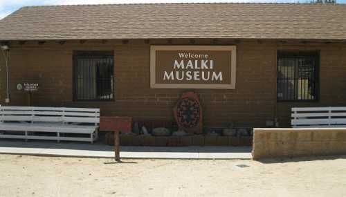 Exterior of the Malki Museum, featuring a welcome sign and benches in front of a rustic building.