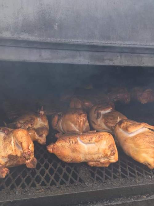 A smoky grill filled with several whole chickens cooking evenly on a metal rack.