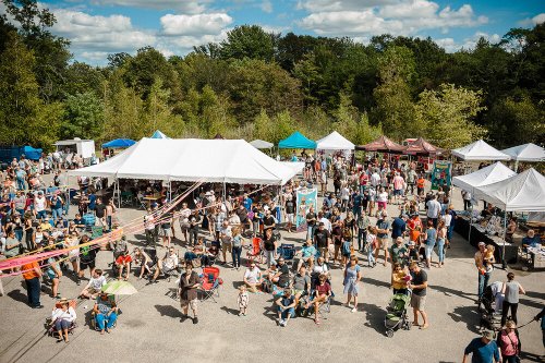 A bustling outdoor market with numerous tents, vendors, and a large crowd enjoying the event under a blue sky.