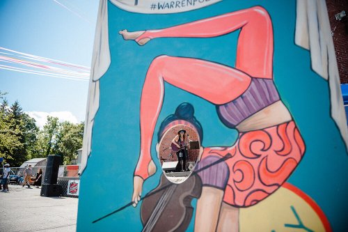 A colorful mural features a woman in a yoga pose, with a person posing through a cutout in the artwork.