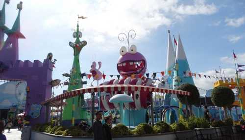 Colorful amusement park scene featuring whimsical structures and a large, cartoonish monster in a bright sky.