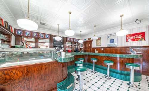 A vintage diner interior featuring a green marble counter, chrome stools, and retro decor with Coca-Cola signage.