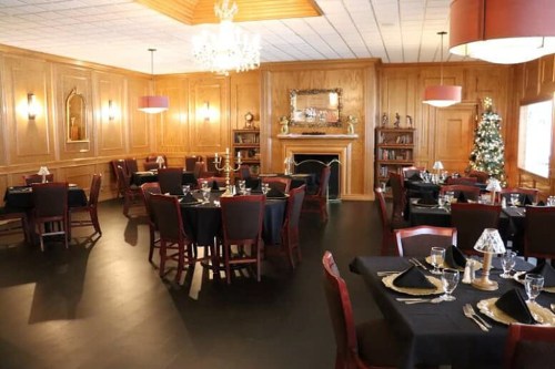 Elegant restaurant interior with wooden walls, black tablecloths, and festive decorations, including a Christmas tree.