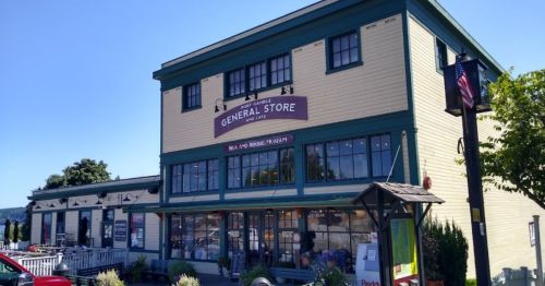 A charming general store with a museum sign, featuring large windows and a bright blue sky above.