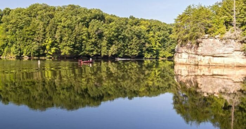 A serene lake surrounded by lush green trees, with a small boat reflecting on the calm water.