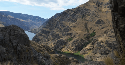 A scenic view of a winding river surrounded by rugged, dry mountains under a partly cloudy sky.