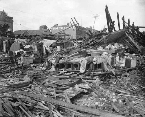 A devastated landscape of debris and ruins, with scattered furniture and remnants of buildings after a disaster.