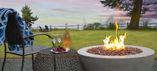 A cozy outdoor scene with a fire pit, a bottle of champagne, glasses, and a blanket draped over a chair at sunset.
