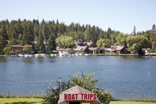Scenic lake view with houses and trees, featuring a sign for boat trips in the foreground.