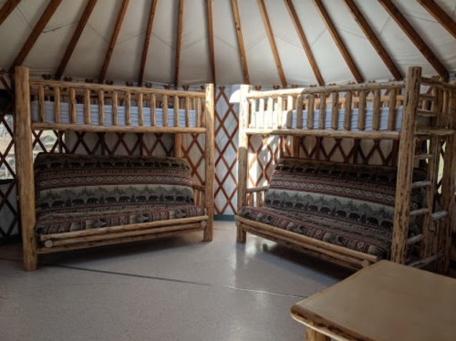 Interior of a yurt featuring two sets of wooden bunk beds and two couches with patterned upholstery.