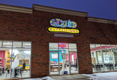 Exterior of Glazed Expressions, a DIY art studio, with an "OPEN" sign and colorful signage on a brick building.