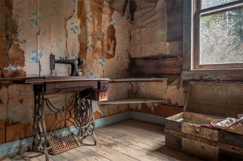 An old, dusty room with peeling wallpaper, a vintage sewing machine, and a weathered trunk in the corner.