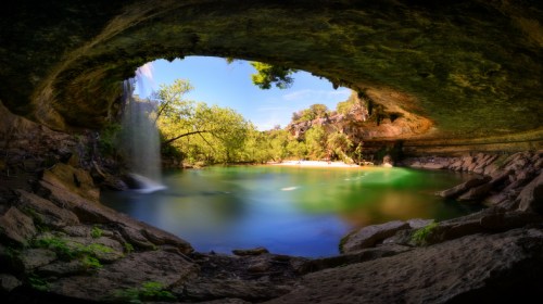 A serene view of a waterfall cascading into a tranquil pool, framed by rocky overhangs and lush greenery.