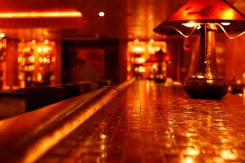 A dimly lit bar with a polished countertop and warm, glowing lamps, creating an inviting atmosphere.