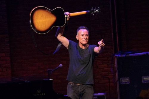 A musician holds up a guitar while pointing at the audience during a live performance on stage.