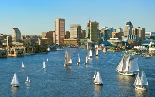 A scenic view of a city skyline with sailboats on a river under a clear blue sky.