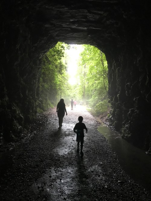 A silhouette of a child running towards light in a misty tunnel, with two figures walking in the background.
