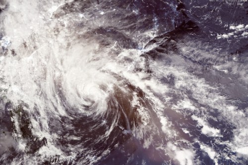 Satellite image of a swirling hurricane over the ocean, surrounded by clouds and atmospheric patterns.