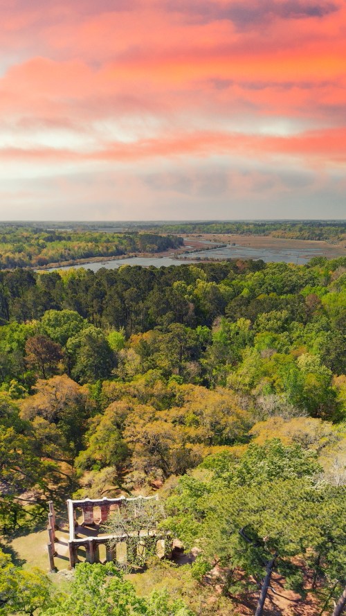 Aerial view of lush green trees and a serene lake under a colorful sunset sky.