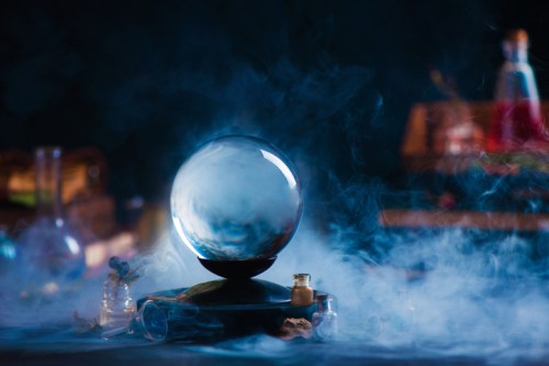 A crystal ball sits on a dark surface, surrounded by smoke and various glass vials in a mystical setting.