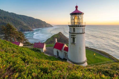 A scenic lighthouse on a cliff overlooking the ocean, surrounded by lush greenery and a sunset sky.