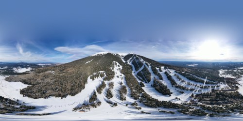 A panoramic view of a snow-covered mountain with ski trails and a clear blue sky.
