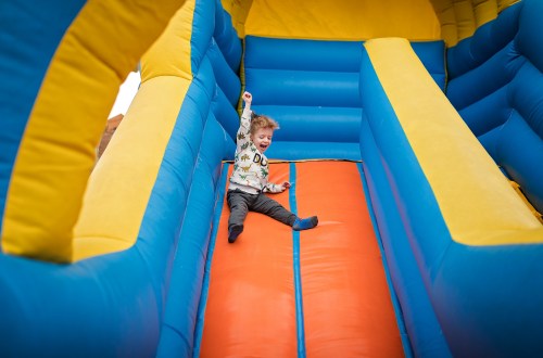 A young child joyfully slides down a colorful inflatable slide at a playground.